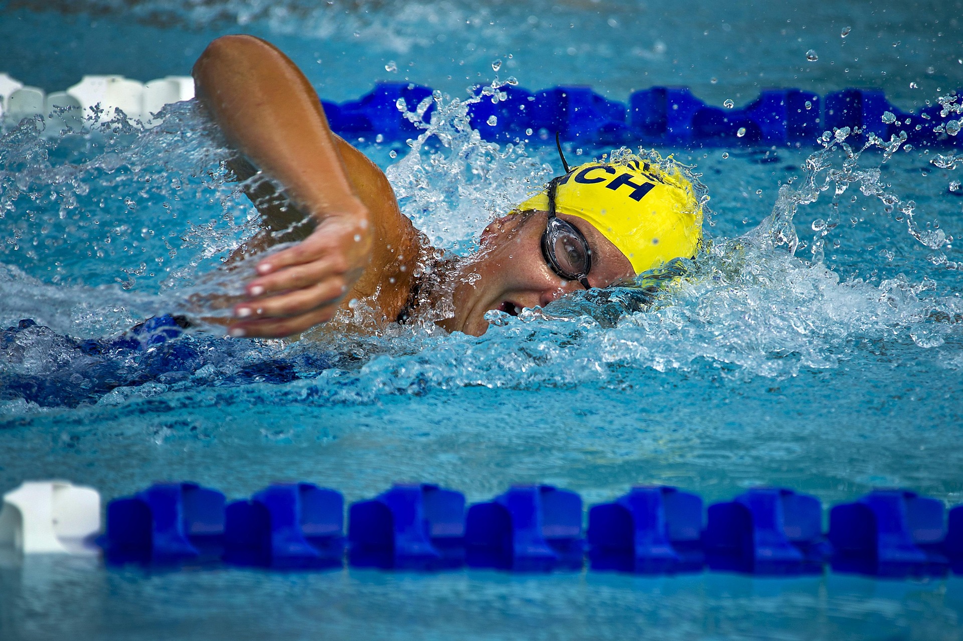 A female swimmer gliding through a blue pool lane during a race, water splashing around her arms.
